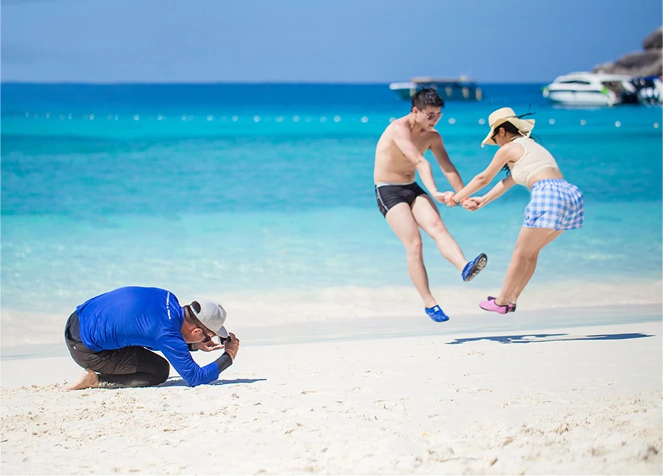 Photographer taking pictures of a couple jumping on a white sand beach